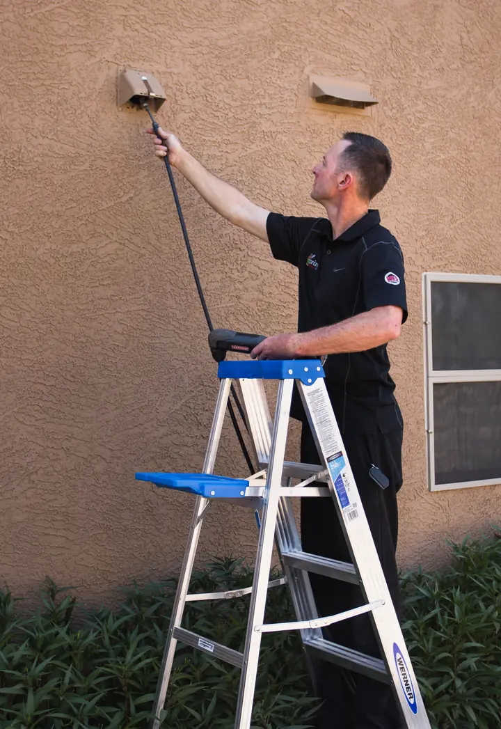 Technician on a ladder cleaning an exterior dryer vent