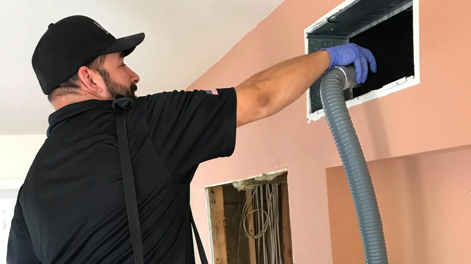 Technician cleaning an air duct register with a vacuum hose