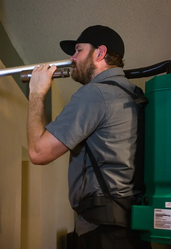 Technician cleaning a ceiling vent with a backpack HEPA vacuum